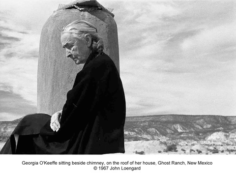 Georgia O'Keeffe sitting beside chimney, on the roof of her house, Ghost Ranch, New Mexico.
